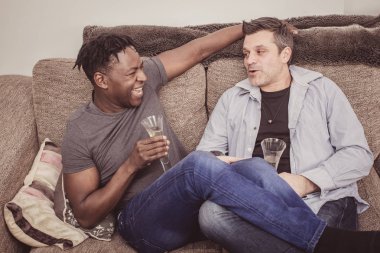 Interracial gay çift evde kanepede biraz şampanya keyfini çıkarın.. 