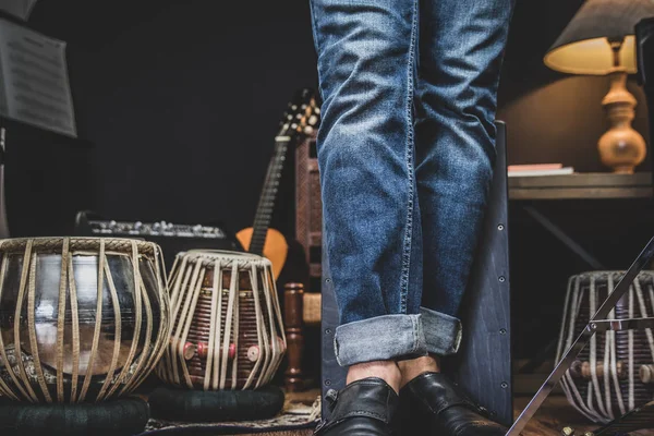 A stylish musician in denim and double monk shoes plays the Cajon, a Peruvian drum used commonly with Spains Flamenco dance.