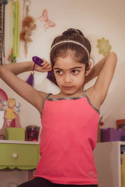 School age British Asian girl getting her hair ready in front of a mirror.