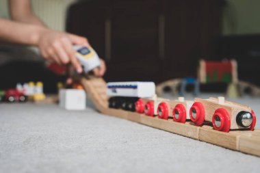 Okul çağındaki çocuklar evlerinde halının üzerine ahşap bir oyuncak tren rayı inşa ediyorlar..