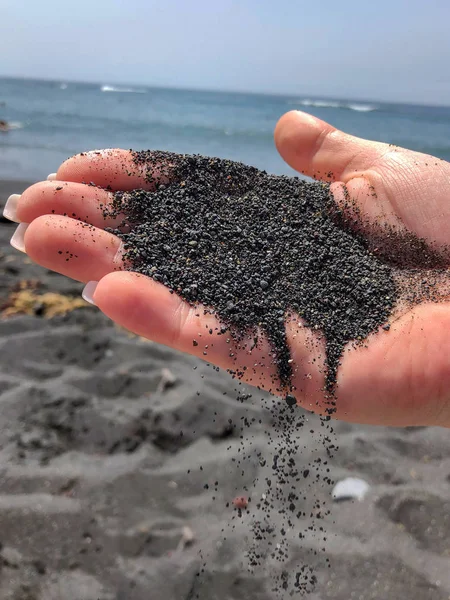 woman hand holding black sand on the volcanic black sand beach