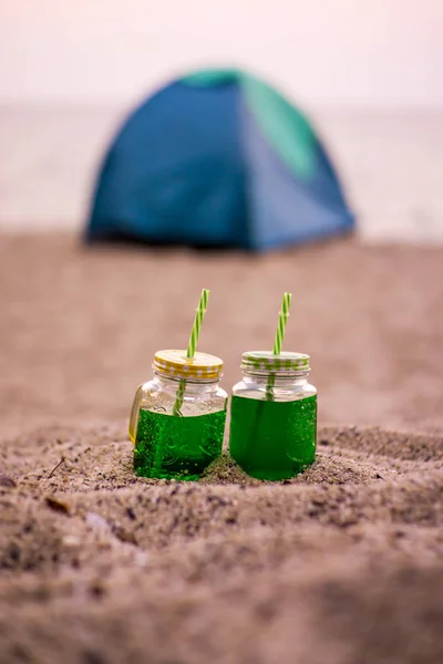 Dos bebidas de pareja amigables con el medio ambiente en la playa con una tienda de campaña —  Fotos de Stock