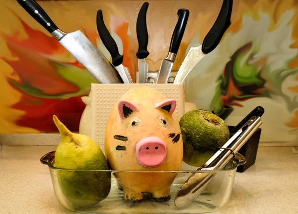 funny ceramic pig in a tray for frying, surrounded by vegetables and kitchen appliances, fills the kitchen with humor.