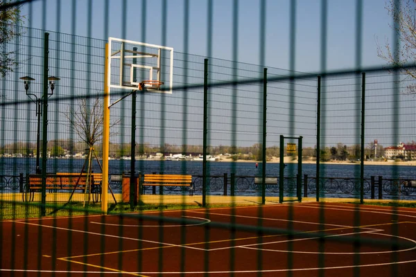 a sports field for playing basketball covered with a safety net is in a city park on the banks of the river