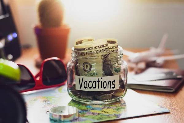 Vacation budget concept. Money for vacations savings in a glass jar with compass, passport, sunglasses, credit card and aircraft toy on world map