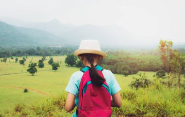 Girl with backpack walking in the field with mountain view during summer at Ranong Province, Thailand.