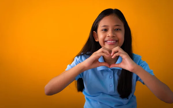Smiling young asian girl in blue shirt showing heart shape with — Stock Photo, Image