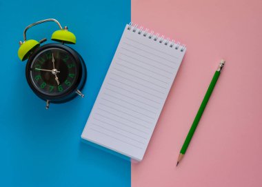 Pembe üzerinde izole yeşil kalem ve alarm saati ile açık Notebook