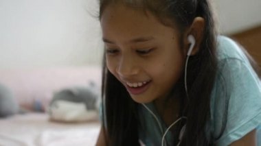 Kız akıllı telefonda en sevdiği şarkıyı dinlerken ve yatakta kulaklıkla müziğin tadını çıkarırken şarkı söylerken.