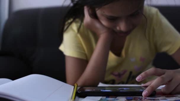 机の上で宿題をしながら携帯電話を使用して若い女の子 技術と教育の概念 — ストック動画