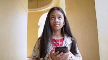 Chino portekiztarzı bina koridorunda yürürken kulaklıkile cep telefonundan müzik dinleuzun saçlı sevimli kız.