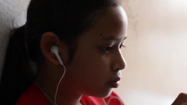 Küçük kız kulaklık ile cep telefonundan müzik dinlerken ve evde oturan.