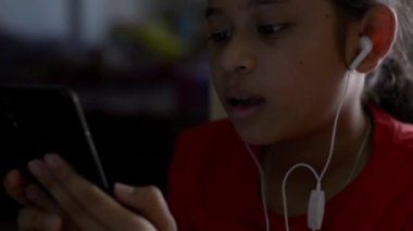 Küçük kız kulaklık ile cep telefonundan müzik dinlerken ve evde oturan.