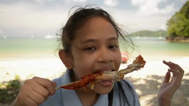 Mała Dziewczynka Jedzenia Pyszne Grillowane Skrzydło Kurczaka Pod Cieniu Plaży — Wideo stockowe