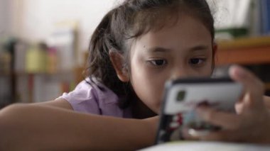 Evde çalışma masasında cep telefonundan video kullanarak ve izlerken küçük sevimli asya kız.