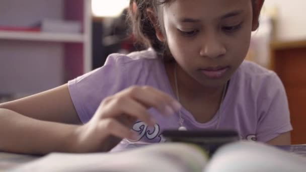 自宅の学習机で携帯電話からビデオを使用して見て少しかわいいアジアの女の子 — ストック動画