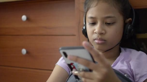 小阿辛女孩使用手机与耳机和在家观看视频 — 图库视频影像
