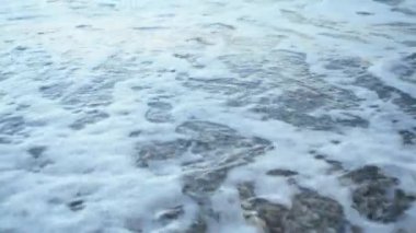 Sahilde birçok küçük taş ile bir deniz kıyısında kırma dalgaları oluşan köpük yakın.