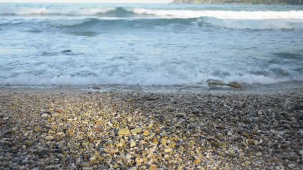 浜辺に多くの小さな石で海岸に壊れる波によって形成された泡のクローズアップ — ストック動画