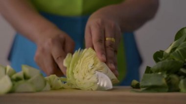 Kadın eli, mutfaktaki masada sağlıklı yiyecekler için ahşap kesim tahtasıyla lahana keserken yakın çekim..