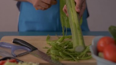 Kadın ellerinin, mutfaktaki masada duran sağlıklı yiyecekler için ahşap kesme tahtasındaki lifleri soyarken yakın plan çekimleri..