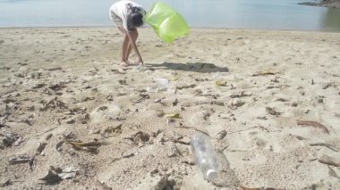 Kumsalda çöpleri yeşil plastik torbaya dolduran genç bir kız, plajda plastik şişeler toplanıyor, plajı temizleyen gönüllü, çevre bilinci kavramı.