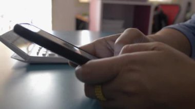 Evdeki masada akıllı telefon kullanan bir kadın cep telefonuna mesaj yazıyor. Evden çalış..