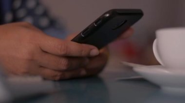 Evdeki masada akıllı telefon kullanan bir kadın cep telefonuna mesaj yazıyor. Evden çalış..