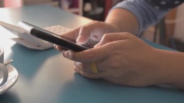 Evdeki masada akıllı telefon kullanan bir kadın cep telefonuna mesaj yazıyor. Evden çalış..