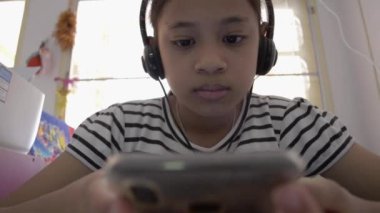 Evde kulaklıkla akıllı telefondan video izleyen sevimli Asyalı kız..