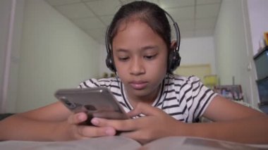 Evde kulaklıkla akıllı telefondan video izleyen sevimli Asyalı kız..