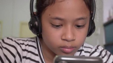 Evde kulaklıkla akıllı telefondan video izleyen sevimli Asyalı kız..