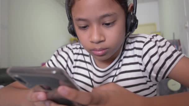 可爱的亚洲女孩在家里用耳机从智能手机观看在线视频 — 图库视频影像