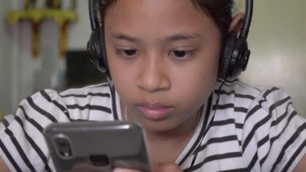 Roztomilé Asijské Dívka Sledování Online Videa Chytrého Telefonu Sluchátky Doma — Stock video