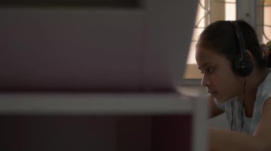 Karantina sırasında evde cep telefonuyla oyun oynarken kulaklık takan güzel Asyalı bir kız COVID-19 salgınıyla karantina sırasında masada. Hobiler ve Boş Zamanlar konsepti. Döndürme çekimi.