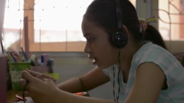 Karantina sırasında evde cep telefonuyla oyun oynarken kulaklık takan güzel Asyalı bir kız COVID-19 salgınıyla karantina sırasında masada. Hobiler ve Boş Zamanlar konsepti.