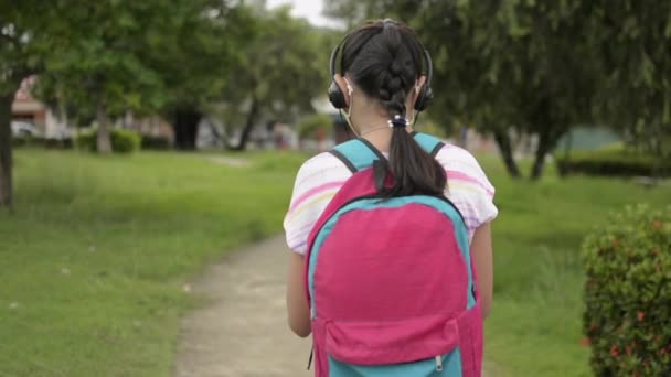 Achteraanzicht Van Aziatisch Basisschoolmeisje Beschermend Gezichtsmasker Met Koptelefoon Wandelen Een — Stockvideo