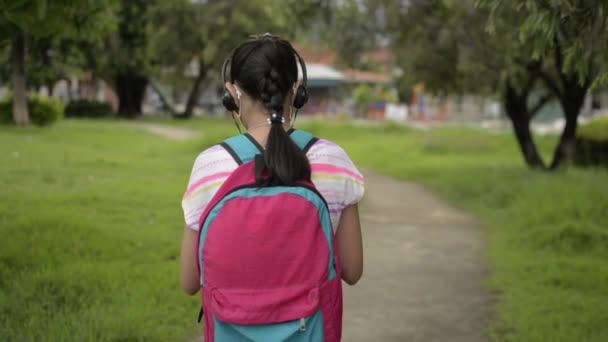 헤드폰을 공원을 산책하고 아시아인 중학교 여학생의 뒷모습 핸드폰으로 가방을 코로나 — 비디오