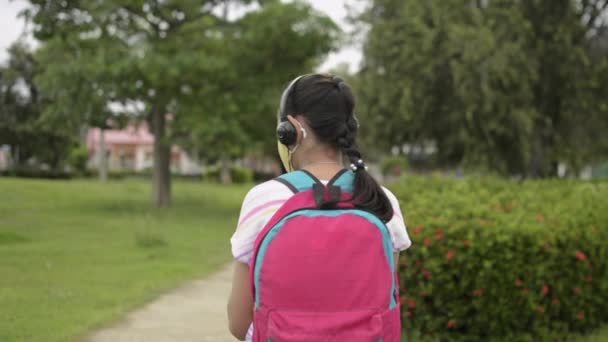 Bakifrån Asiatisk Grundskoleflicka Skyddande Ansiktsmask Bär Hörlurar Och Promenader Allmän — Stockvideo