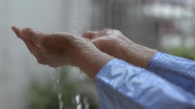 Mavi yağmurluk giymiş, evin önünde yağmurla oynayan kadınların ellerini kapat. Doğada aşk kavramı.