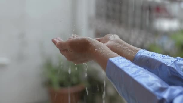 雨の女性の手にドロップを閉じます 家の前で雨と青のレインコートで女の子を再生します 自然の概念への愛 — ストック動画
