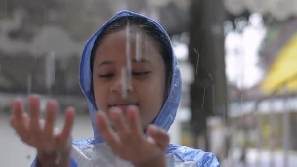 青いレインコートで愛らしい若いアジアの女の子が家の前で雨と遊ぶのを楽しむ 自然の概念における子供時代と愛 — ストック動画