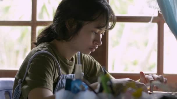 在家里的办公桌上放着数码平板电脑的亚洲女青少年 穿着休闲装的可爱女孩坐在窗边 在桌上做作业 网上社交用数字设备发短信 — 图库视频影像