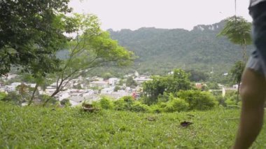 Asyalı kadın turistin arka görüntüsü çimlerde yürüyor ve vadideki phang nga şehrinin güzel manzarasını görmek için cep telefonuyla tepeden fotoğraf çekiyor. Seyahat güzergahı. Atışı kaldırıyorum. Tayland.