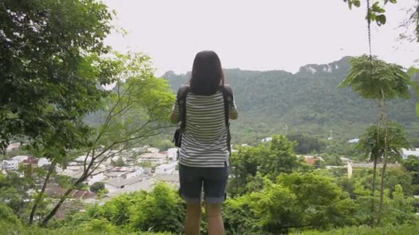 芝生の上を歩いて 携帯電話で丘の上から写真を撮るアジアの女性観光客の背面ビューは 渓谷のパンガー市の美しい景色を見ることができます 目的地へ 射撃を解除する — ストック動画