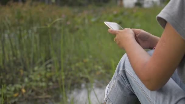 Asian Woman Casual Dress Sitting Grass Natural Pond Texting Mobile — Stock Video