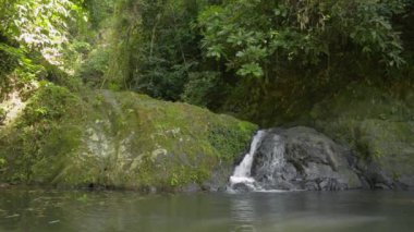 Dağlardan akan küçük bir şelale. Tropikal yağmur ormanlarında güneş ışığı altındaki doğal gölete akan güzel tatlı su. Namtok Raman Orman Parkı. Phang Nga bölgesi. Tayland.