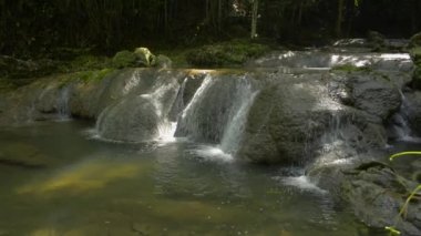 Tatlı su çağlayandan kayalara doğru akar verimli bir ormandaki güneş ışığı altındaki doğal bir gölete. Döndürme atışı. Sa Nang Manora orman parkı. Phang Nga Eyaleti. Tayland