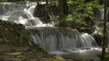 Bereketli bitki örtüsü arasında kayaların arasından akan şelale manzarası. Yağmur mevsiminde tropikal ormanlardaki çağlayanlardan tatlı su hızlı akar. Parallax iğnesi. Sa Nang Manora Orman Parkı. Tayland.