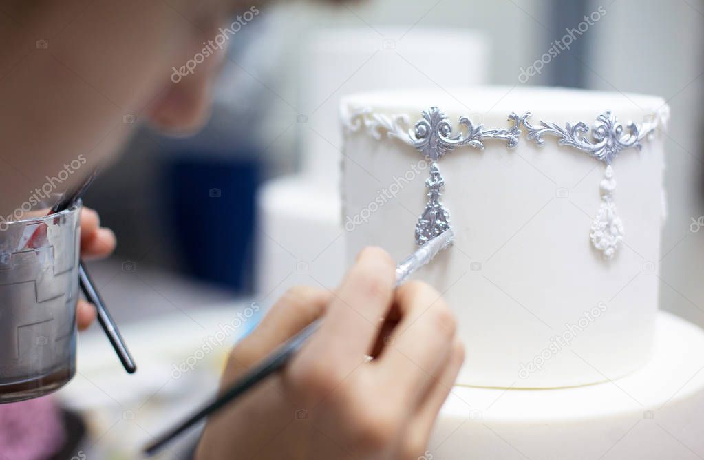 Young lady decorating weeding cake by brush with silver colour